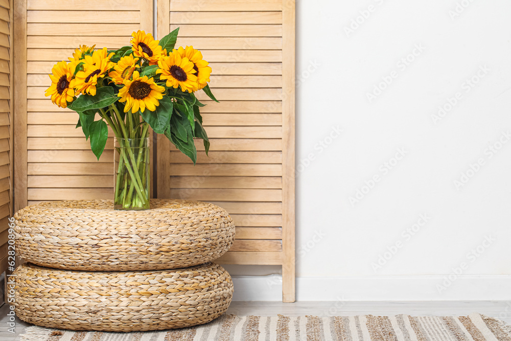 Vase with beautiful sunflowers on wicker mats near folding screen