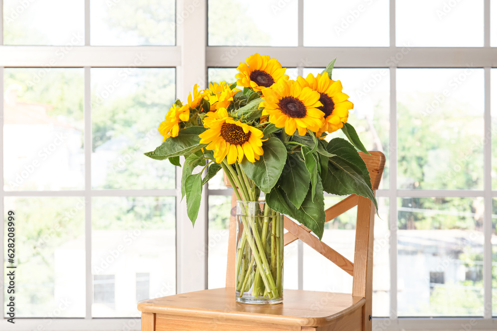 Vase with beautiful sunflowers on stool near big window