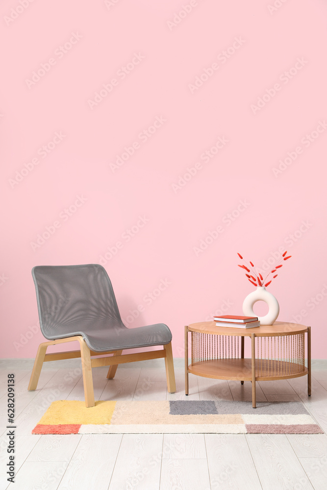 Grey armchair, coffee table and stylish rug near pink wall