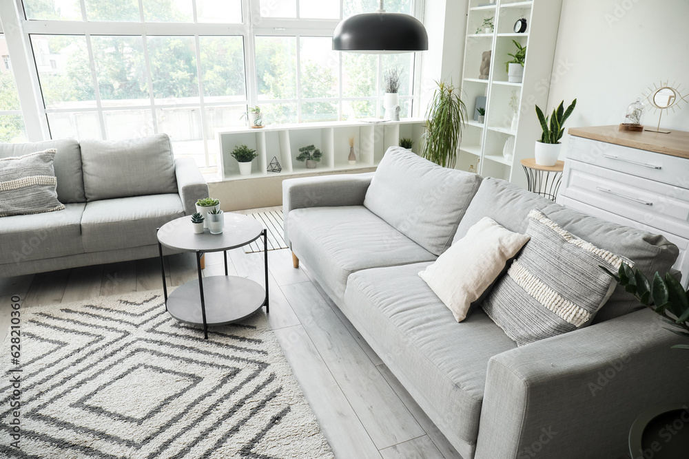 Interior of light living room with cozy grey sofas, coffee table and big window