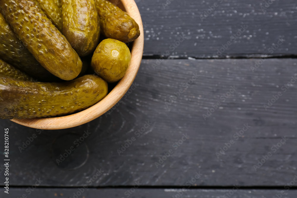 Bowl with pickled cucumbers on black wooden background