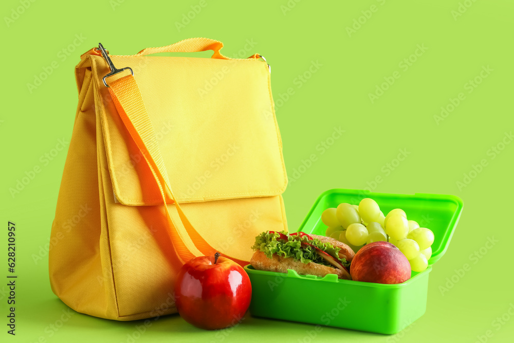 Bag and lunchbox with tasty food on green background