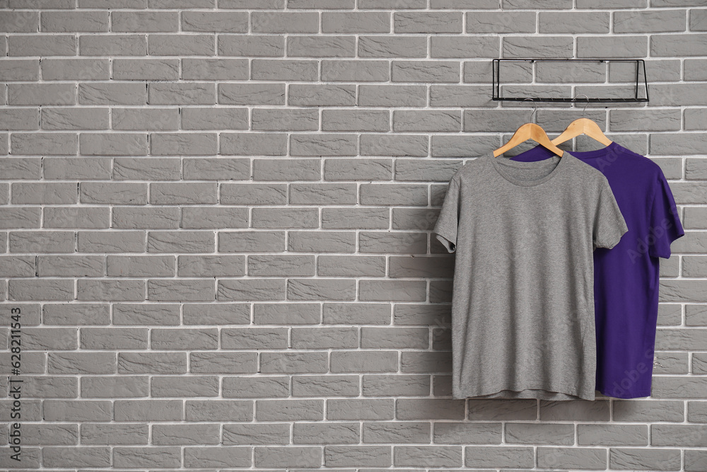 Stylish t-shirts hanging on grey brick wall