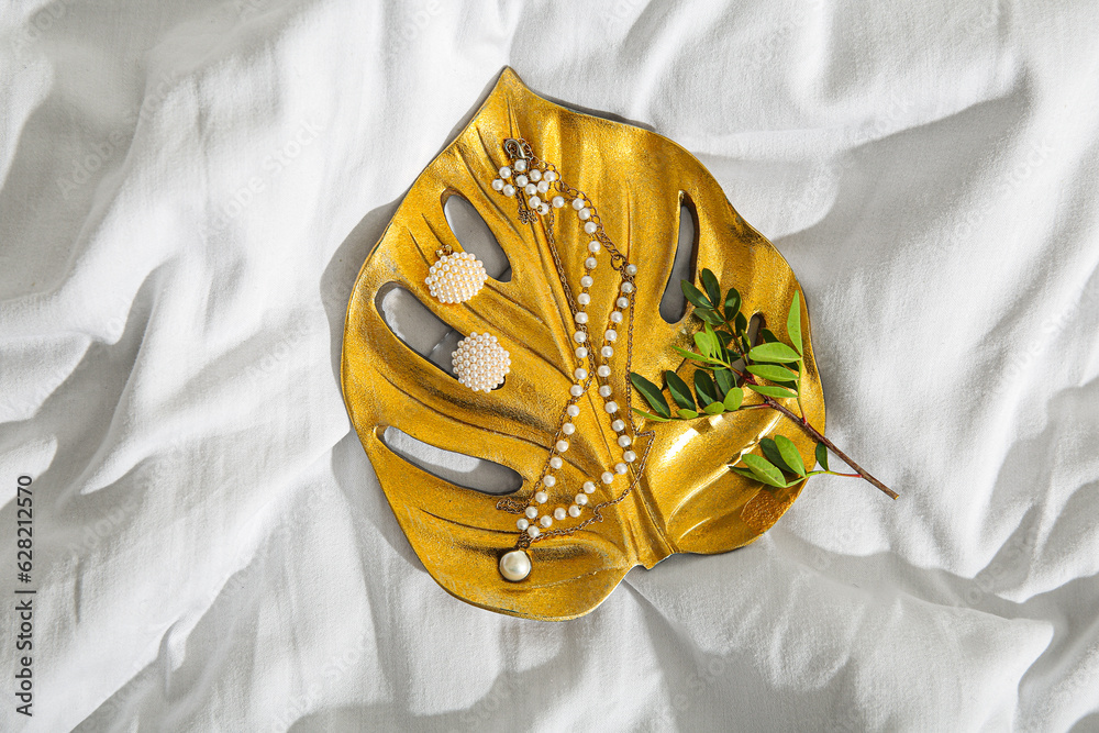 Golden palm leaf tray with beautiful pearl jewelry and plant branch on white cloth