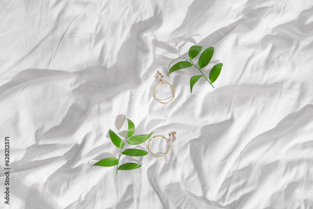 Beautiful golden earrings with plant leaves on white cloth