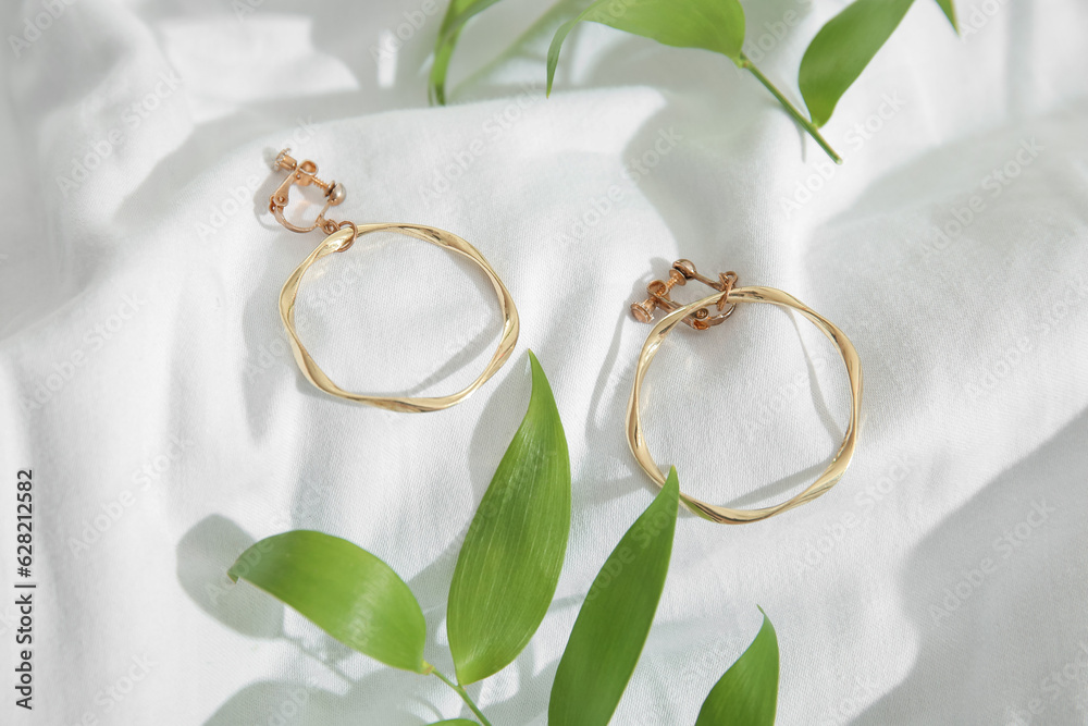 Beautiful golden earrings with plant leaves on white cloth