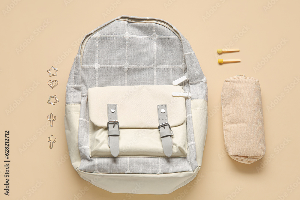 Grey school backpack with stationery on beige background