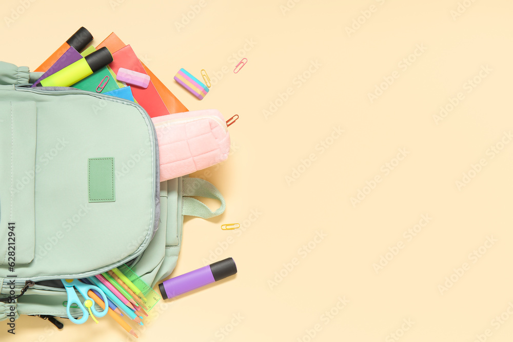 Green school backpack with different stationery on yellow background