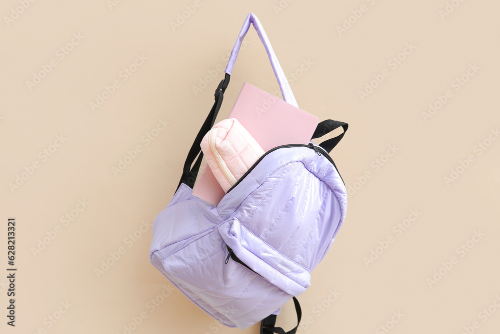 Lilac school backpack with stationery on beige background