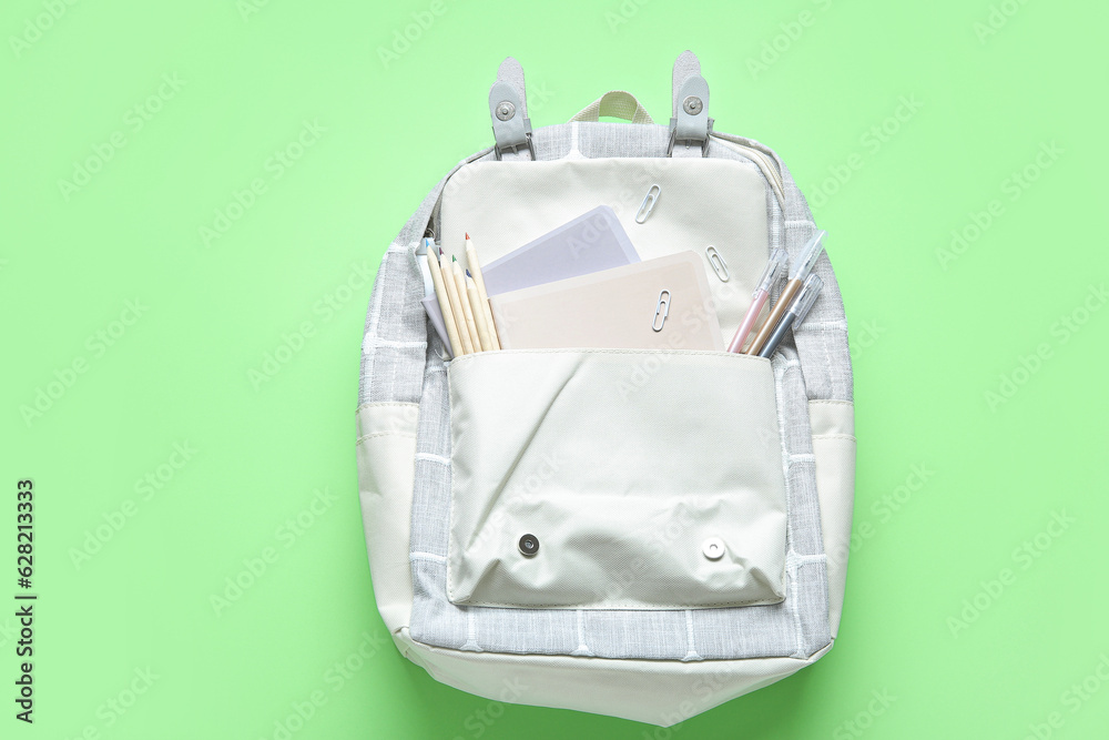 Grey school backpack with different stationery on green background