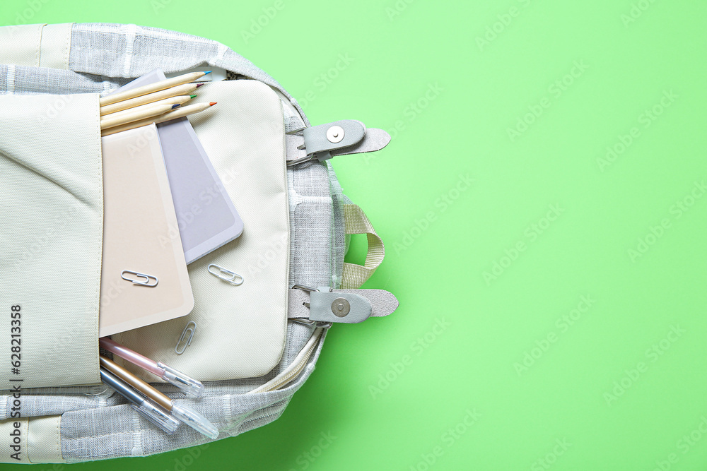 Grey school backpack with different stationery on green background