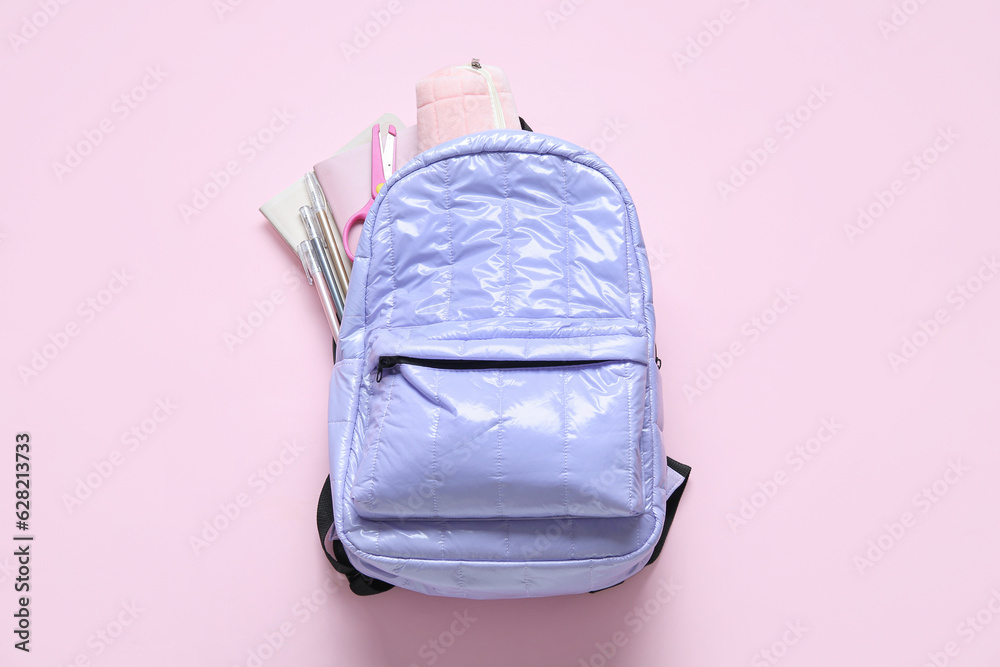 Lilac school backpack with stationery on pink background