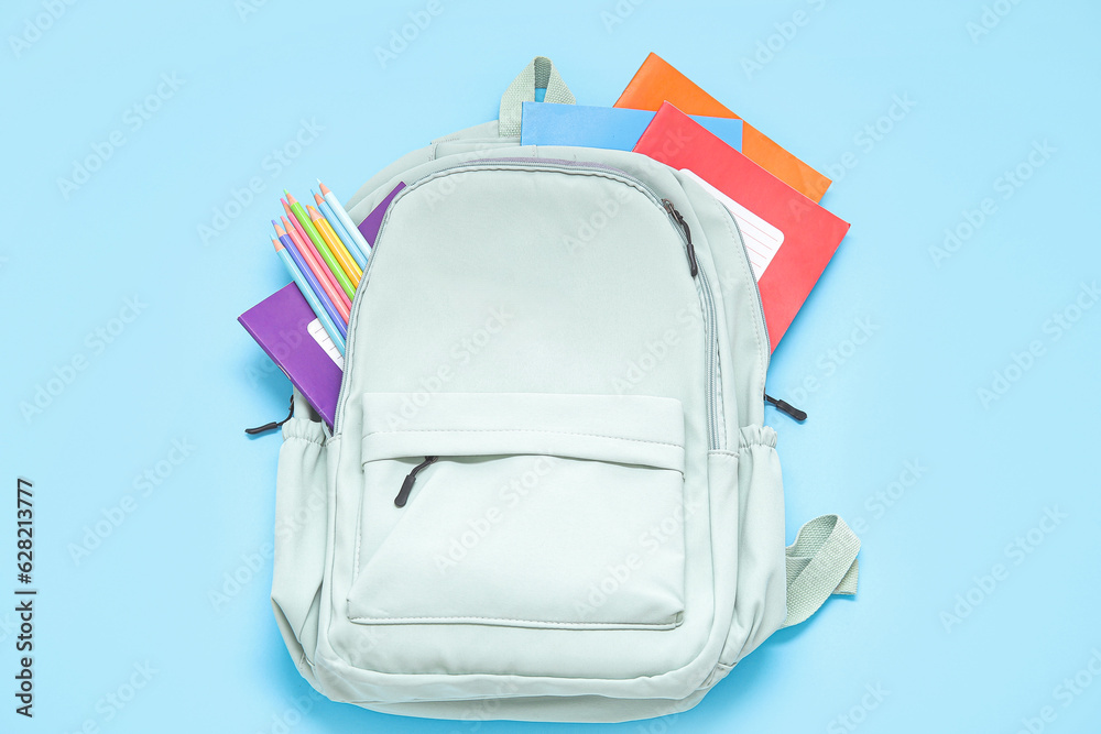 Green school backpack with stationery on blue background