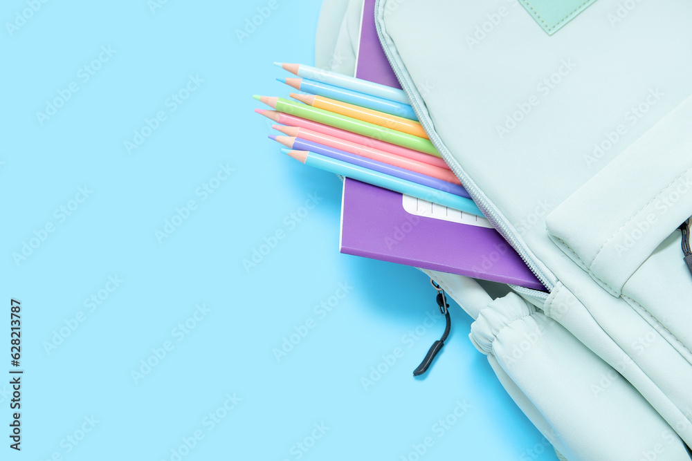 Green school backpack with stationery on blue background