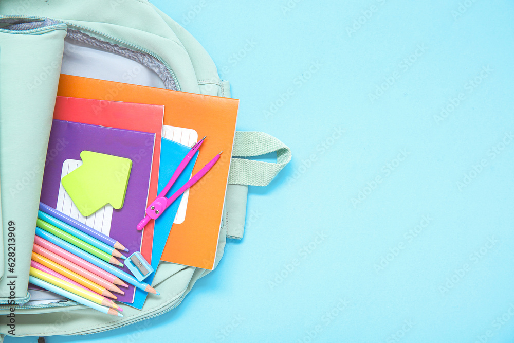 Green school backpack with different stationery on blue background