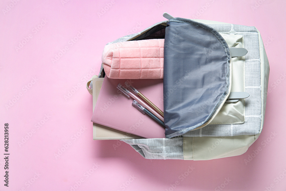 Color school backpack with different stationery on pink background