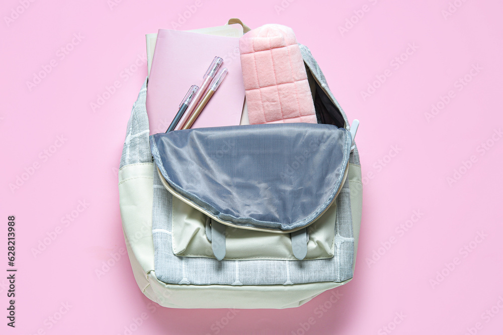 Color school backpack with different stationery on pink background