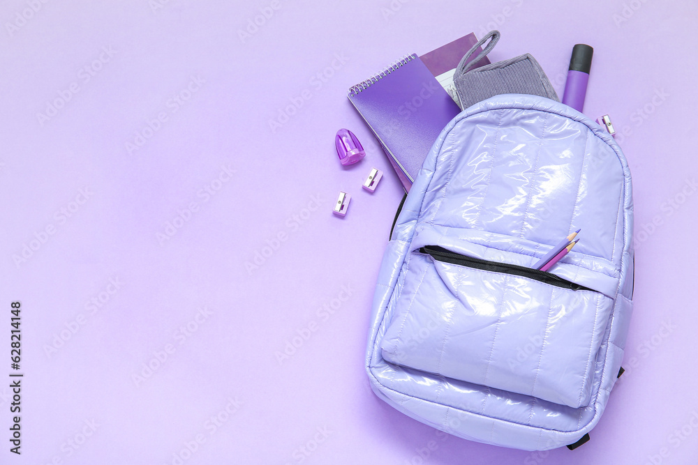 Lilac school backpack with different stationery on purple background