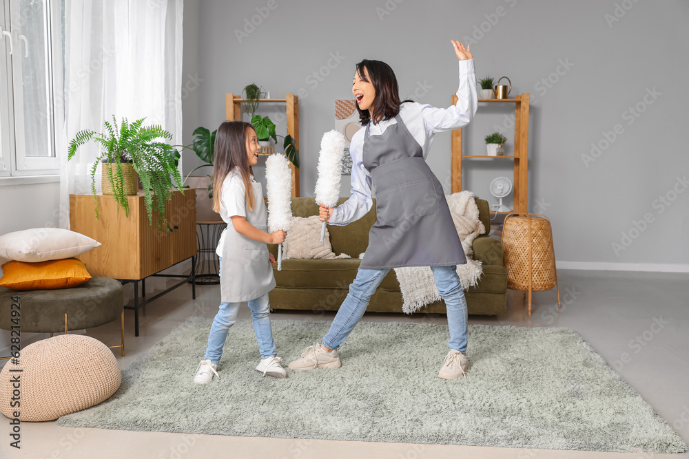 Asian mother with her little daughter dancing while cleaning at home