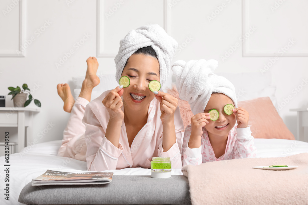 Asian mother with her little daughter and cucumber slices in bedroom