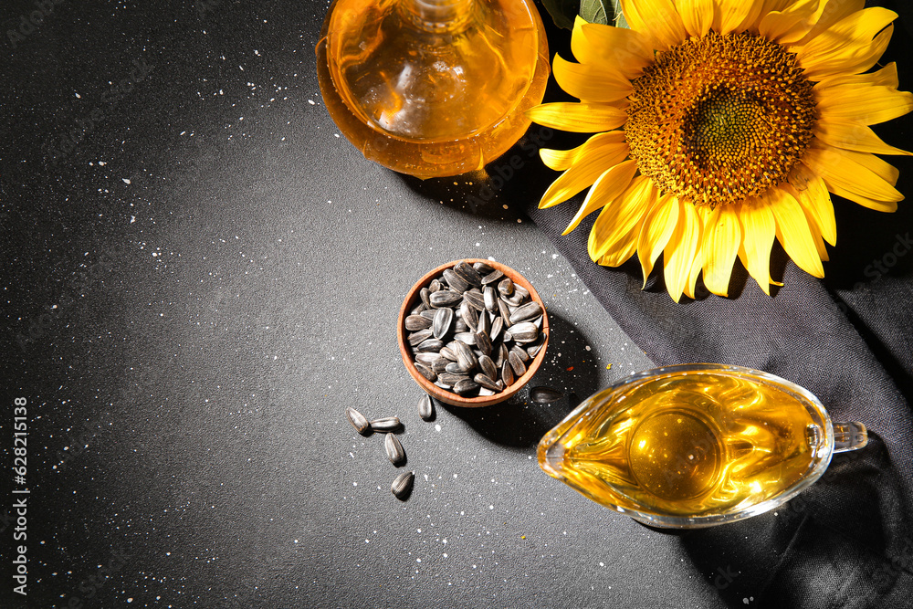 Gravy boat of sunflower oil and wooden bowl with seeds on black background