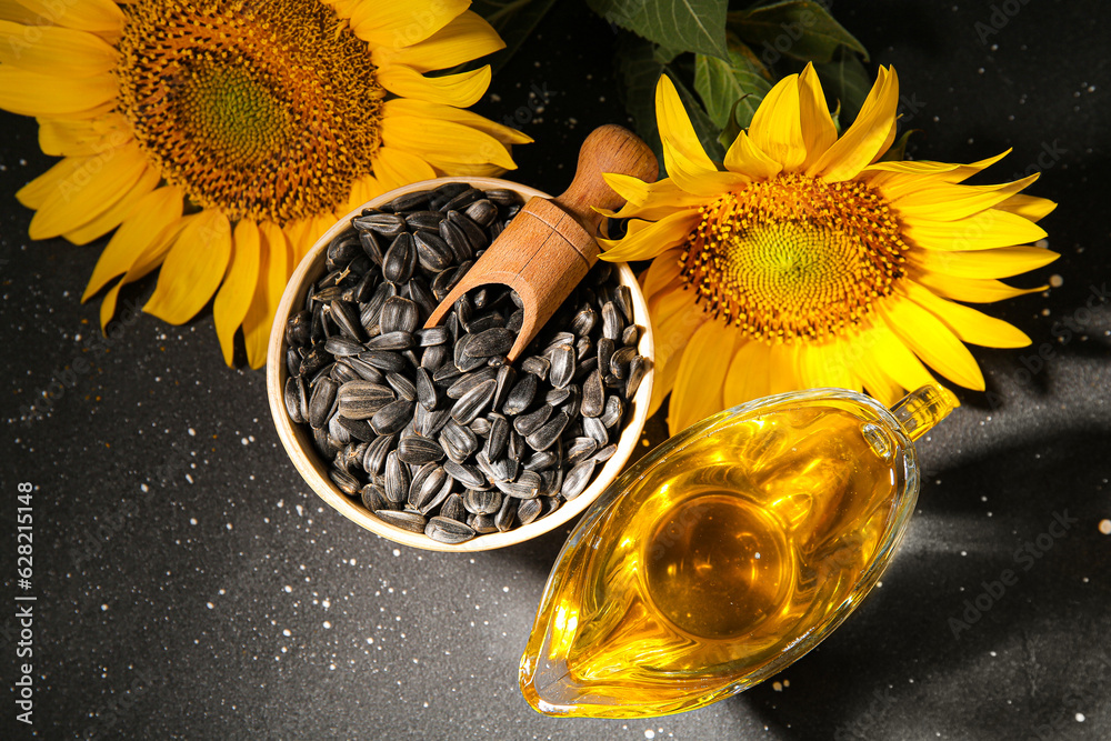 Gravy boat of sunflower oil and wooden bowl with seeds on black background