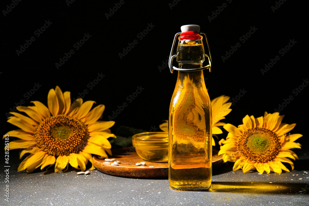 Bottle and glass bowl of sunflower oil with seeds on black background