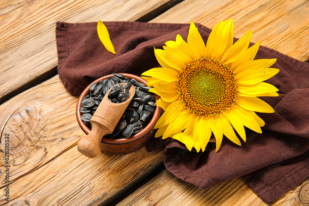 Beautiful sunflower and bowl with seeds on wooden background