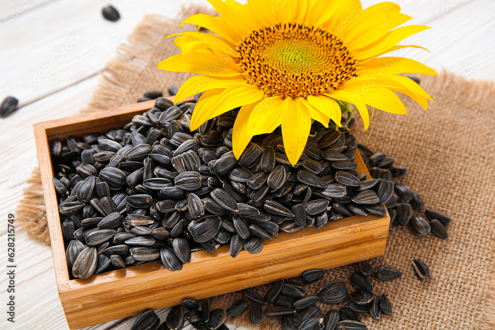 Beautiful sunflower and box with seeds on white wooden background