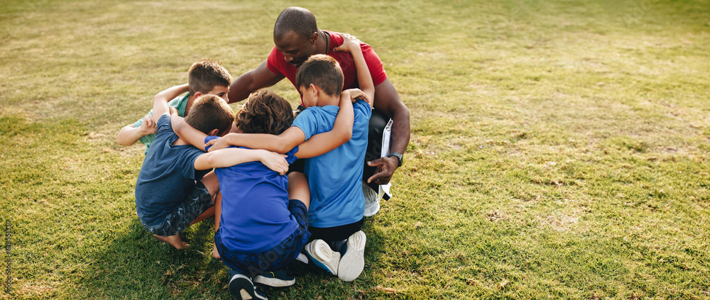 School kids huddling with their coach in a sports ground