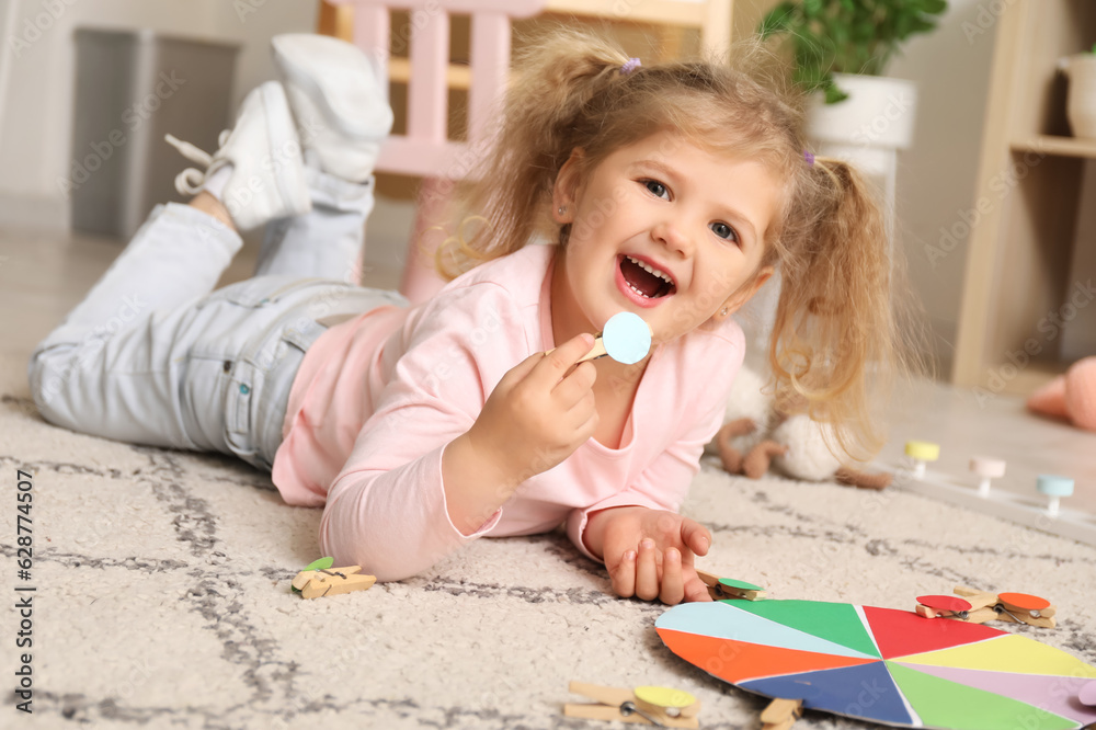 Cute little girl playing matching game with clothespins on floor at home