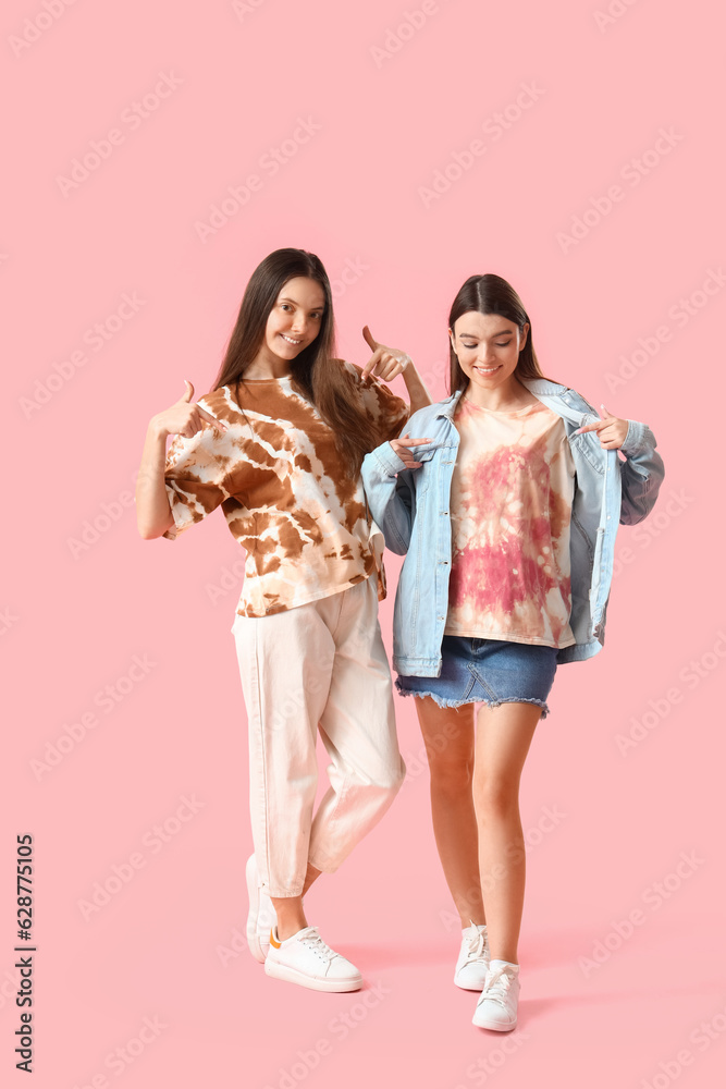 Stylish young women in tie-dye t-shirts on pink background