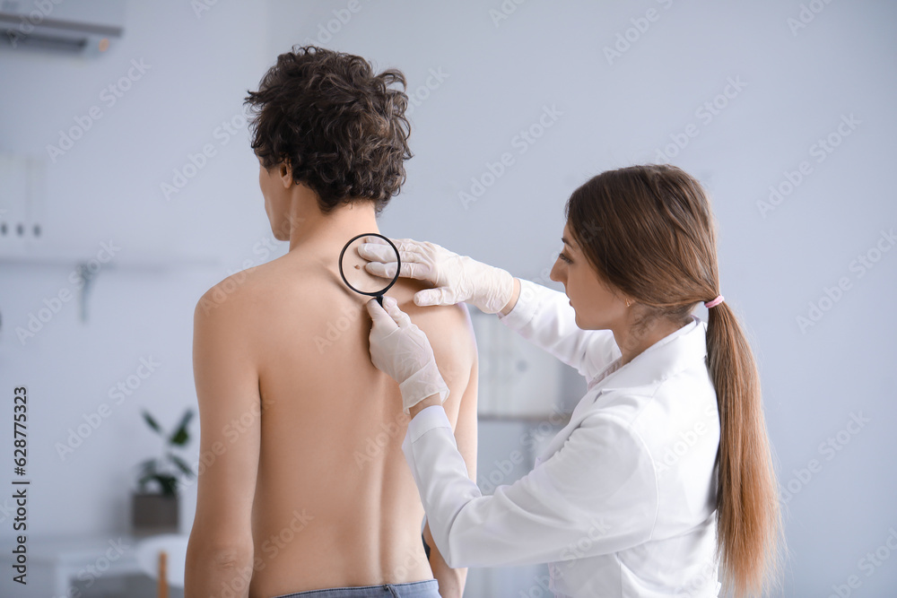 Dermatologist examining mole on young mans back with magnifier in clinic