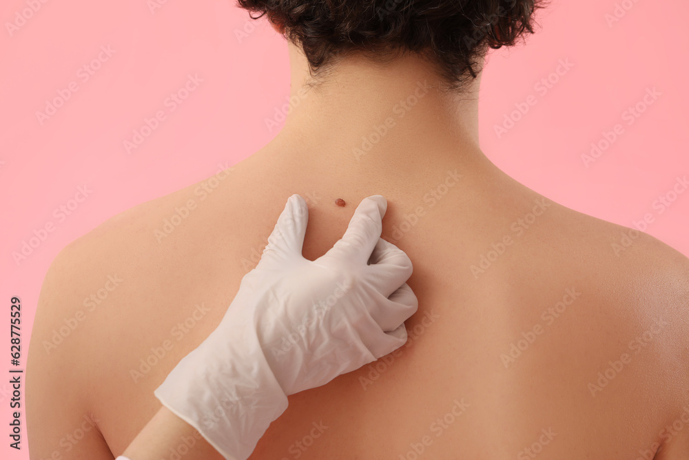 Dermatologist examining mole on young mans back against pink background, closeup