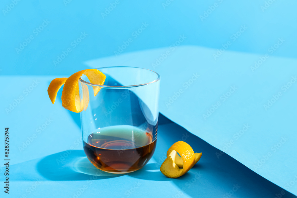 Glass of rum with orange peels on blue background