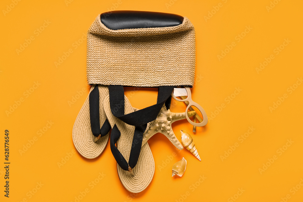 Bag with flip-flops, seashells and sunglasses on red background