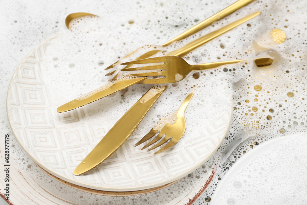 Golden cutlery with plates and foam in water, closeup