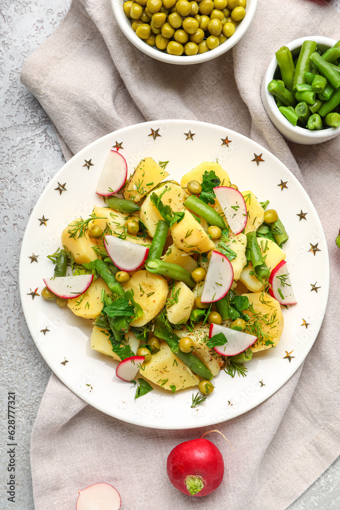 Plate of tasty Potato Salad with vegetables and ingredients on light background