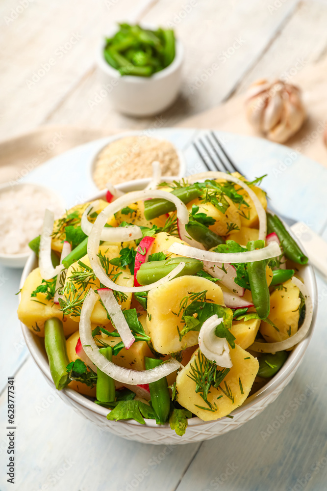 Bowl of tasty Potato Salad with vegetables on light wooden background