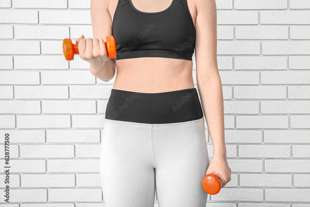 Sporty woman with dumbbells near white brick wall