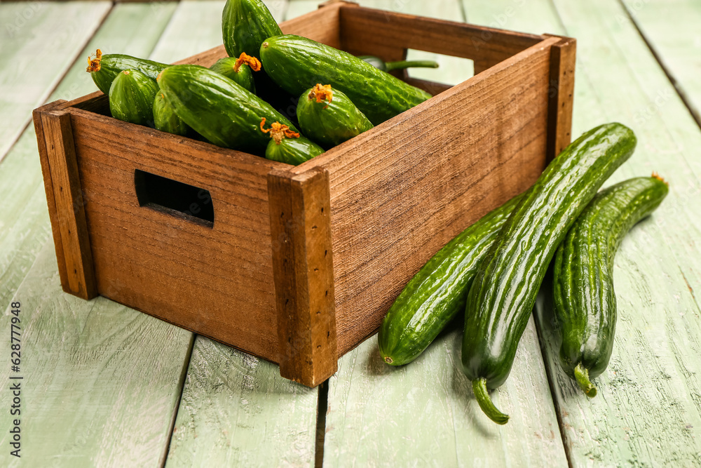 Box with fresh cucumbers on light wooden background