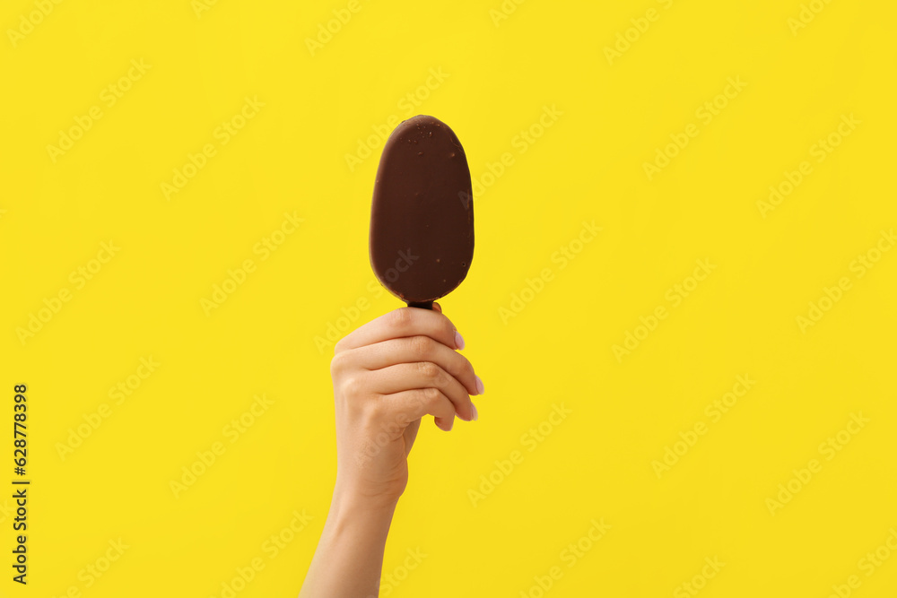 Woman holding delicious chocolate covered ice cream on stick against yellow background