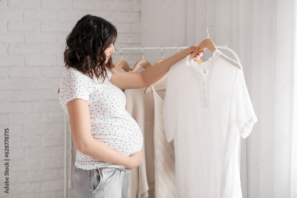 Young pregnant woman with clothes in bedroom