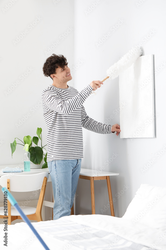 Young man cleaning painting with pp-duster in bedroom