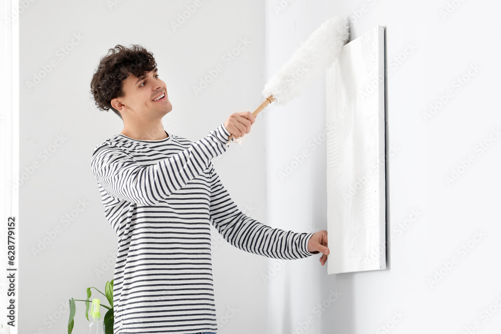 Young man cleaning painting with pp-duster in bedroom