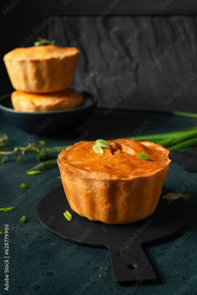 Board with tasty meat pot pie on dark background