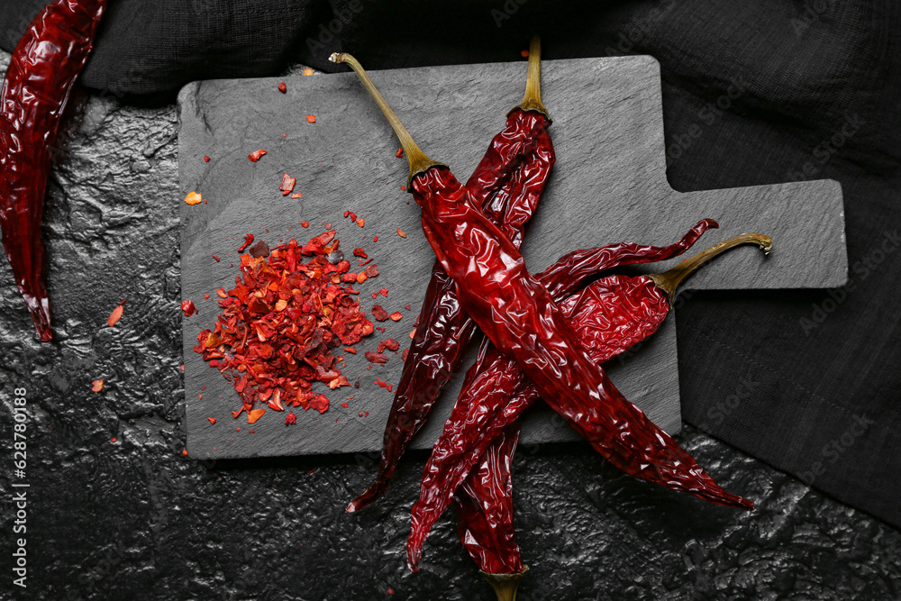 Board with dry chili and ground peppers on dark background