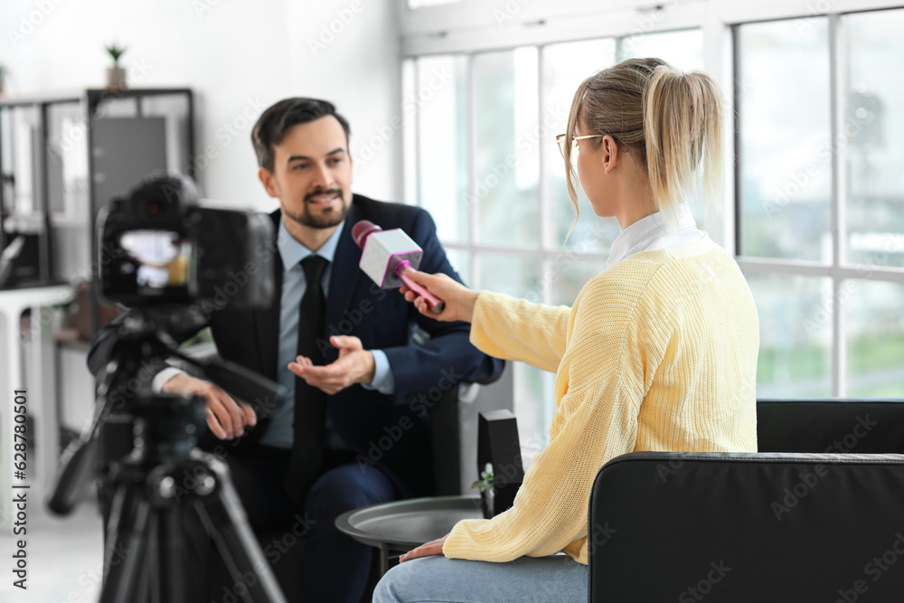 Female journalist with microphone having an interview with man on camera screen in office, closeup