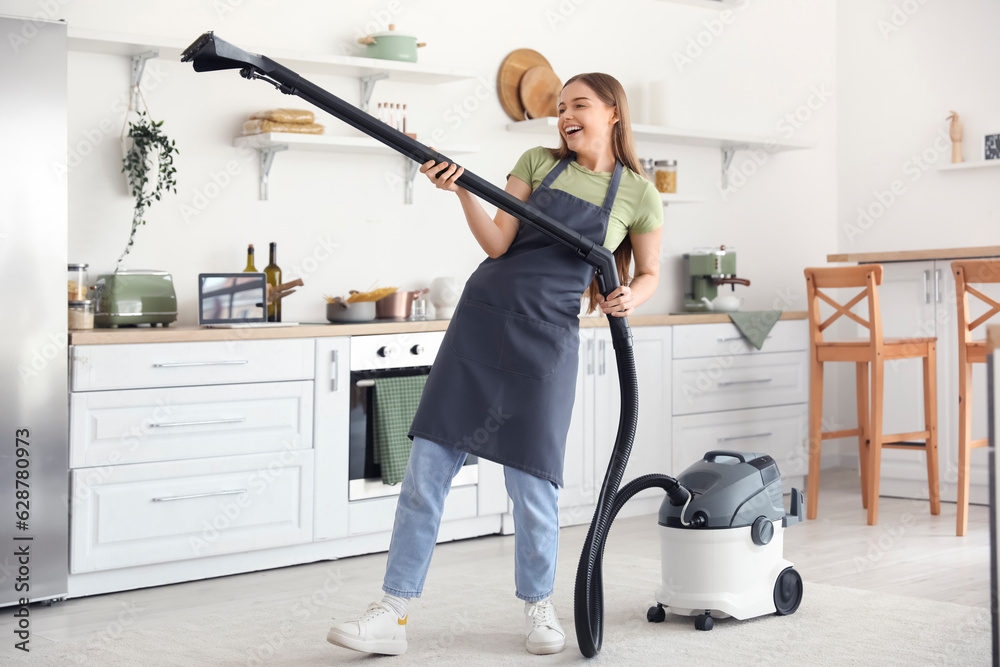 Young woman with vacuum cleaner dancing in kitchen