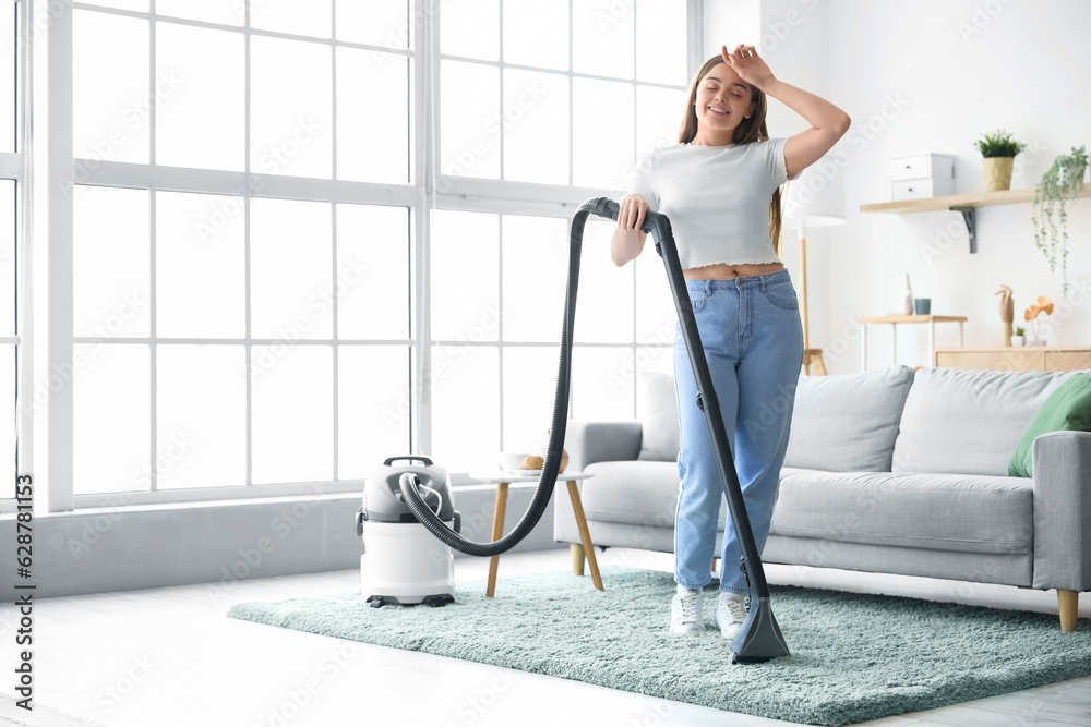 Tired young woman hoovering carpet at home